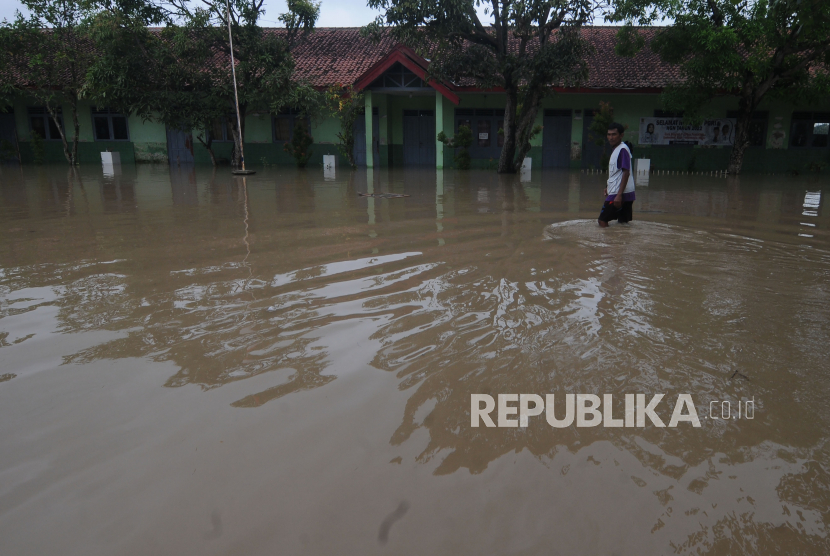 Warga melintas di halaman sekolah dasar negeri yang terendam banjir (ilustrasi) 