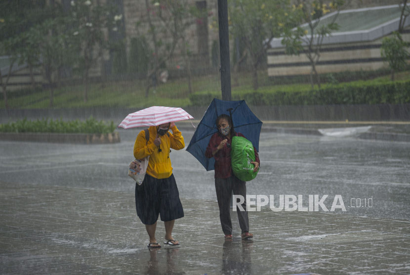 Warga menggunakan payung saat hujan mengguyur Jakarta.
