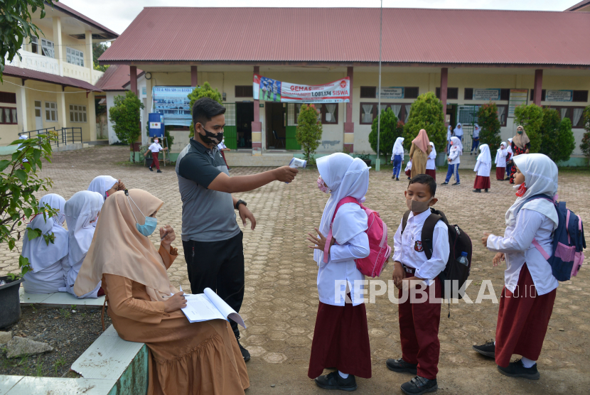 Guru melakukan pengecekan suhu badan dan penggunaan masker murid pascapenutupan sekolah terkait pelanggaran protokol kesehatan di salah satu Sekolah Dasar Negeri, Desa Pango Raya, Banda Aceh, Aceh, Selasa (12/1). Aceh menjadi daerah yang dikecualikan dari SKB tiga menteri tentang larangan pemaksaan atribut keagamaan tertentu dalam seragam sekolah. (ilustrasi)