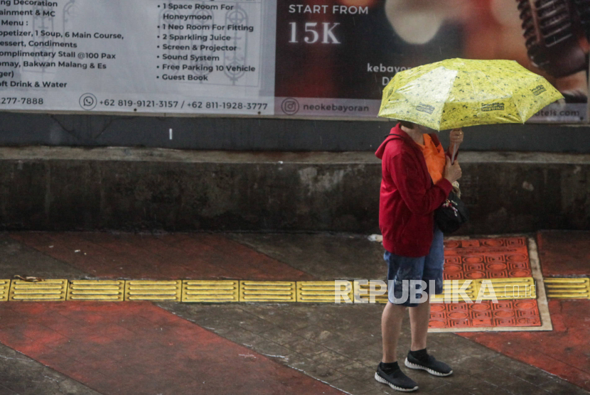 Warga menggunaka payung saat hujan mengguyur sebuah kawasan 