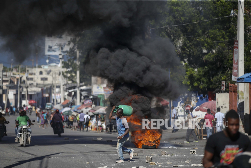 Seorang pria membawa tabung gas melewati ban yang dibakar sebagai bagian dari protes terhadap kekurangan gas di Port-au-Prince, Haiti, Kamis, 21 Oktober 2021.