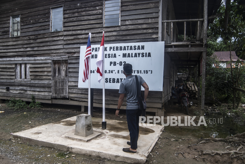 Wisatawan berdiri di atas patok perbatasan Indonesia-Malaysia di Pulau Sebatik, Senin (13/9/2021). Daerah tersebut memiliki rumah yang didalamnya terletak di dua negara, dimana ruang tamu di Indonesia sementara ruang baca dan dapur di Malaysia. 