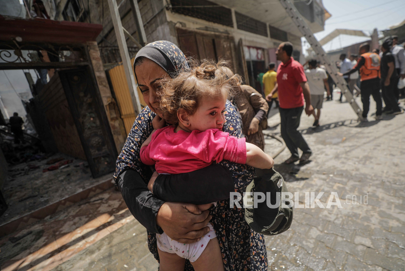 Seorang wanita Palestina yang menggendong seorang anak melarikan diri dari lokasi kejadian setelah serangan udara Israel di kamp pengungsi Al Nuseirat, Jalur Gaza tengah, 29 April 2024.