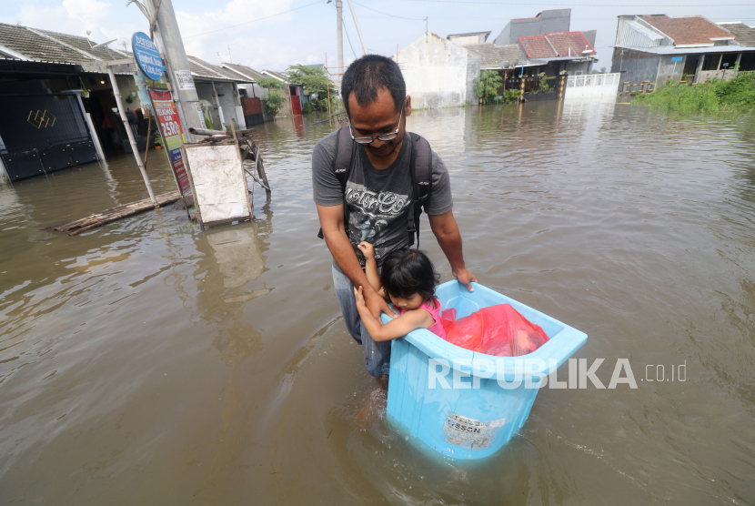 Seorang ayah bersama anaknya menerobos baniir yang merendam kawasan Desa Kwadungan di Kediri, Jawa Timur, Kamis (7/1/2021). Ratusan rumah di wilayah itu terendam banjir usai hujan deras dan meluapnya sungai yang membawa air dari daerah yang lebih tinggi. 