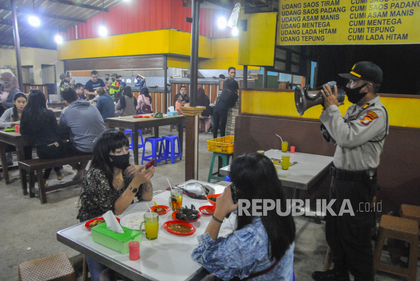 Petugas Kepolisian dengan menggunakan pengeras suara menginformasikan kepada pengunjung tempat makan tentang aturan jam malam di Bekasi, Jawa Barat