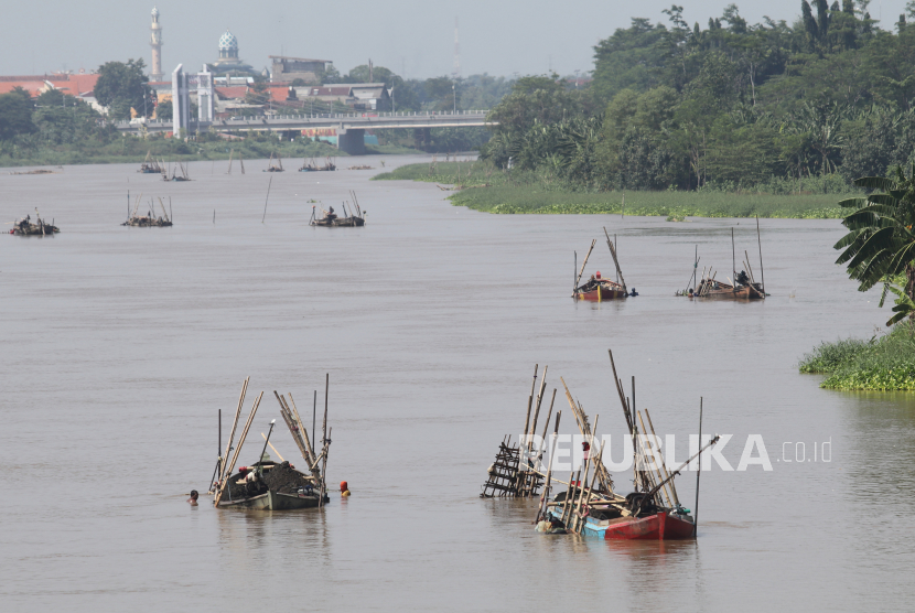 Pekerja menambang pasir menggunakan perahu dengan latar belakang jembatan Brawijaya di aliran sungai Brantas, Kota Kediri, Jawa Timur. Sungai ini pun dipenuhi dengan sampah mikropalstik. 