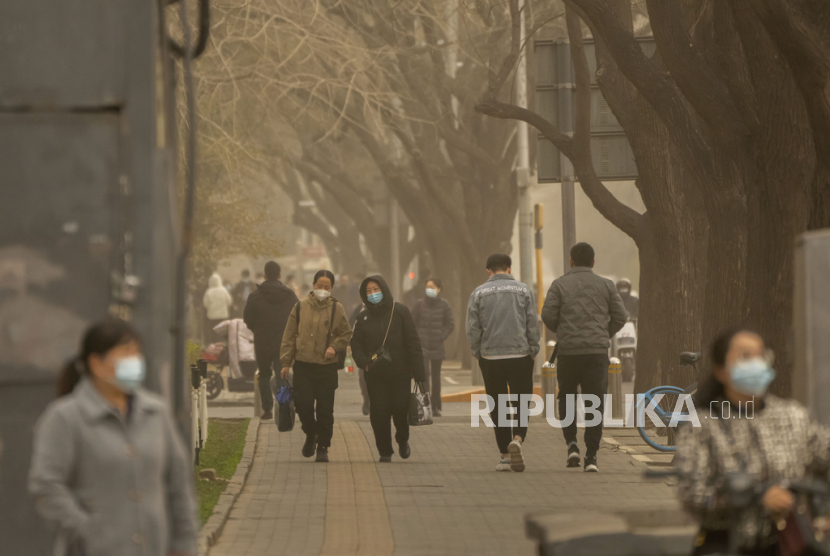 Orang-orang yang memakai masker berjalan di sepanjang jalan di kawasan pusat bisnis di Beijing. Badai debu dan pasir membuat indeks kualitas udara melonjak di ibu kota China pada Rabu pagi.
