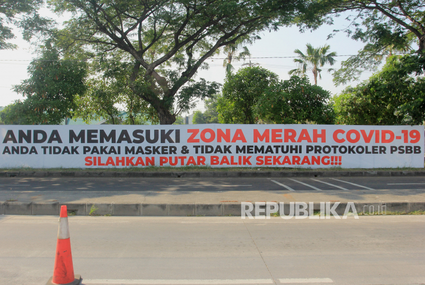 Sebuah spanduk bernada peringatan terpasang di pagar jalan di akses keluar Jembatan Suramadu, Surabaya, Jawa Timur. Pada Ahad (28/6), data pemerintah mencatat kasus positif Covid-19 kembali terbanyak berasal dari Jatim. 