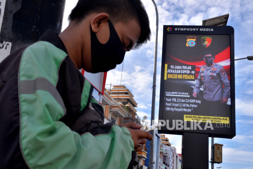 Warga beraktivitas dibawah papan reklame elektronik berisi himbauan ancaman pidana di Jalan Piere Tendean, Manado, Sulawesi Utara, Selasa (21/4/2020). Polda Sulut mensosialiasikan Pasal 178, 212, dan 214 KUHP dan Pasal 14 ayat (1) UU no