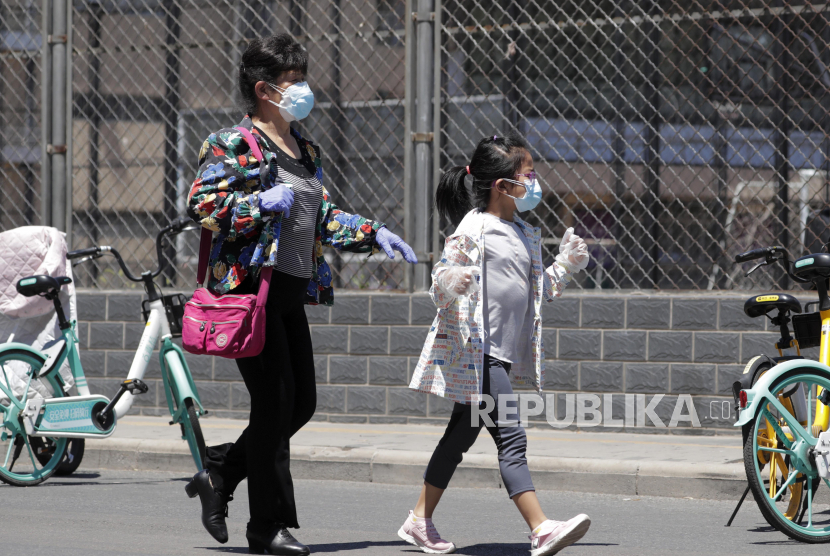 Seorang wanita dan anak-anak mengenakan masker saat berjalan di pasar grosir makanan laut yang ditutup untuk pemeriksaan di Beijing, China, Ahad (14/6). China melaporkan total harian tertinggi kasus virus Corona dalam dua bulan setelah pasar makanan grosir terbesar di ibukota ditutup karena terdapat infeksi lokal