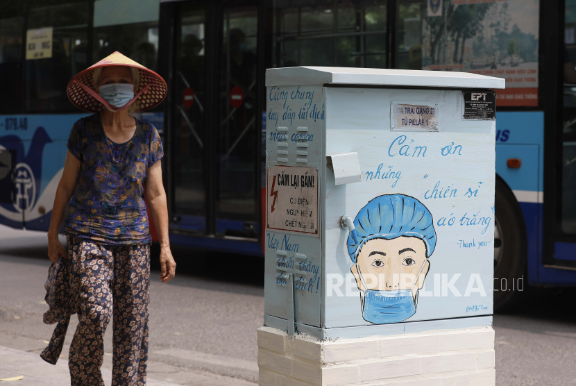 Seorang wanita berjalan melewati kotak listrik yang dicat dengan tema Covid-19 di Hanoi, Vietnam, 07 Juni 2021.