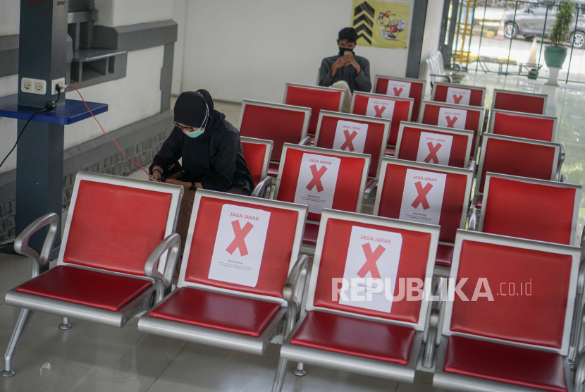 Calon penumpang duduk di kursi tunggu yang diberi penanda jarak aman 