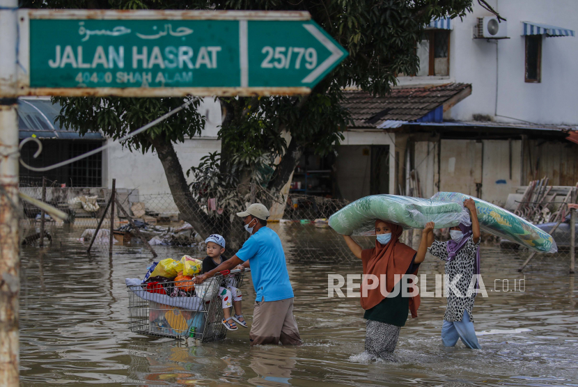Seorang pria (kiri) mendorong troli dengan anak dan barang-barangnya, sementara anggota keluarga lainnya membawa kasur, setelah banjir melanda Taman Sri Muda, distrik Shah Alam, sekitar 40 km dari Kuala Lumpur, Malaysia, 21 Desember 2021. 