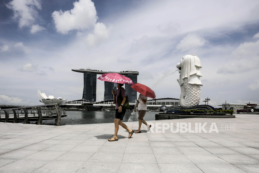 Dua wanita dengan memakai payung berjalan di dekat patung Merlion di Singapura, Senin (6/4). Badan Lingkungan Nasional (NEA) Singapura mencatat panas di negara tersebut mencapai 37 derajat celsius pada Sabtu (13/5/2023).