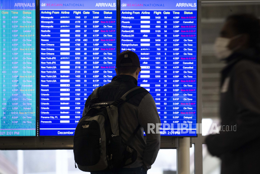  orang melihat papan status penerbangan di Bandara Nasional Ronald Reagan Washington di Arlington, Virginia, AS, 27 Desember 2021. Ribuan penerbangan di seluruh dunia dibatalkan selama akhir pekan Natal dan dilanjutkan 27 Desember, dipicu oleh varian omicron dari Covid-19 .