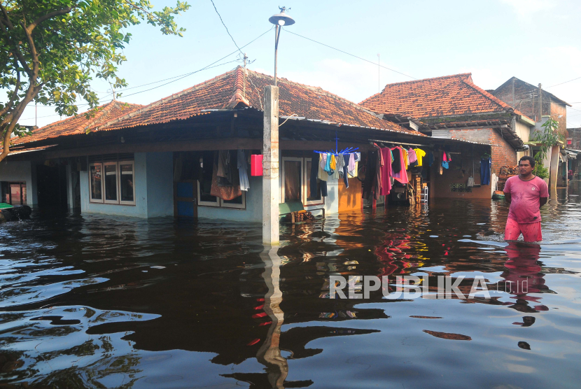 Warga berjalan di depan rumah yang tergenang banjir di Karangturi, Setrokalangan, Kaliwungu, Kabupaten Kudus, Jawa Tengah, Selasa (19/3/2024). 