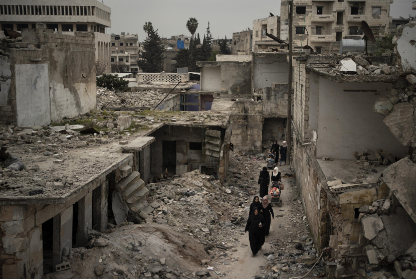 Sejumlah wanita berjalan diantara reruntuhan bangunan yang hancur akibat serangan udara di kota Idlib, Suriah. (AP Photo/Felipe Dana)