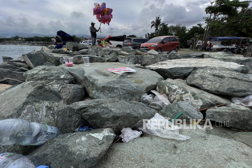 Pengunjung berada di dekat sampah makanan dan minuman yang ditinggalkan di pinggir pantai (ilustrasi) 