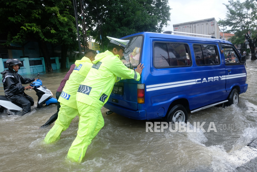 Polisi bersama warga mendorong mobil yang mogok saat melintasi banjir di jalur Pantura, kota Kendal, Jawa Tengah, Sabtu (31/12/2022). Hujan lebat menyebabkan bencana banjir di jalur pantura kabupaten Kendal sehingga arus lalu lintas tersendat . 