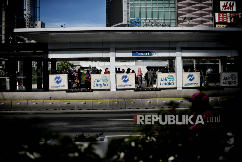 Warga  menunggu angkutan Transjakarta di Jalan Sudirman, Jakarta, Ahad (12/12). Meski aturan PPKM level 3 saat libur Natal dan Tahun Baru 2021  (Nataru) dibatalkan, masyarakat diimbau untuk tetap waspada terhadap ancaman gelombang tiga Covid-19 dengan membatasi mobilitas di tempat kerumunan serta menerapkan protokol kesehatan yang ketat. Republika/Thoudy Badai