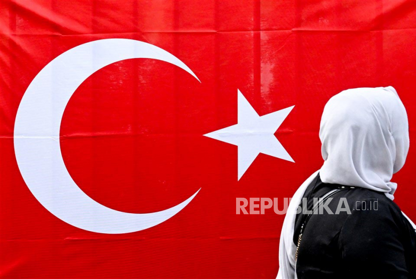 Seorang wanita Turki berdiri di samping bendera Turki dalam antrean di kedutaan Turki untuk memberikan suara dalam pemilihan umum Turki, di Berlin, Jerman, Kamis (27/4/2023). 