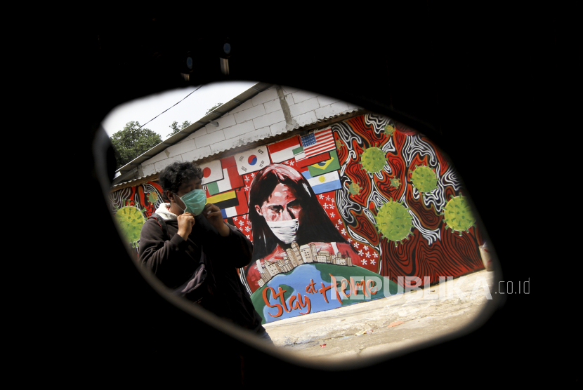Seorang Warga melintas di depan mural bertuliskan Stay At Home di Cipayung, Depok, Jawa Barat, Selasa (14/4/2020). Pemerintah Kota Depok akan menerapkan Pembatasan Sosial Berskala Besar (PSBB) mulai Rabu (15/4) sebagai upaya memutus rantai penyebaran virus corona COVID-19