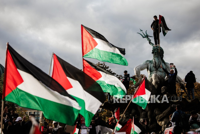 Seorang pengunjuk rasa berpose dengan bendera Palestina di air mancur Neptunus saat aksi solidaritas Palestina, di Berlin, Jerman,  Ahad (5/11/2023).