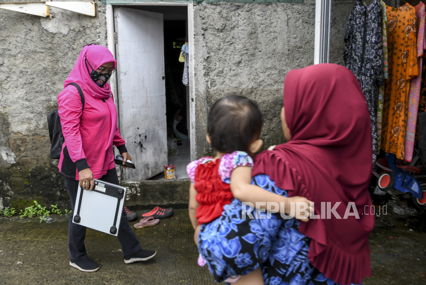 Seorang kader posyandu dengan membawa alat timbang berat badan digital berjalan menuju rumah warga di kawasan Rorotan, Jakarta Utara. 