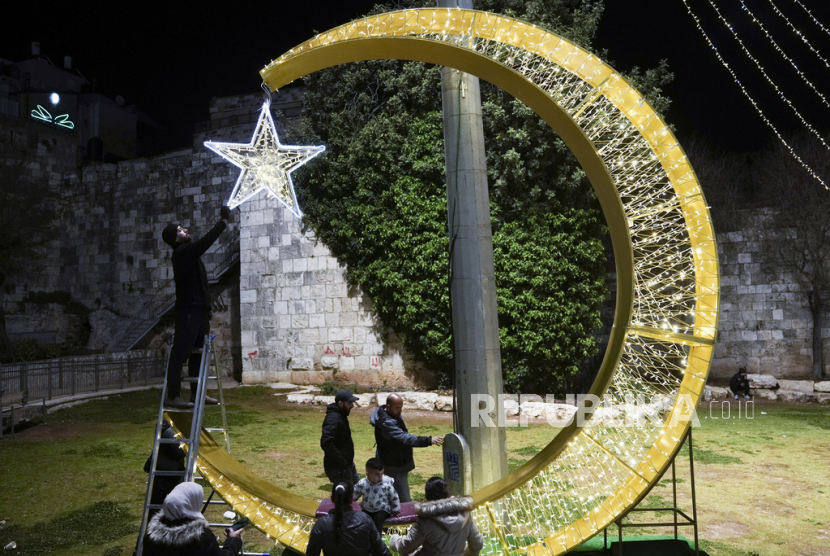  Seorang pria Palestina menggantungkan lampu hias untuk menyambut bulan suci Ramadhan, tepat di luar Kota Tua Yerusalem, Selasa (21/3/2023).