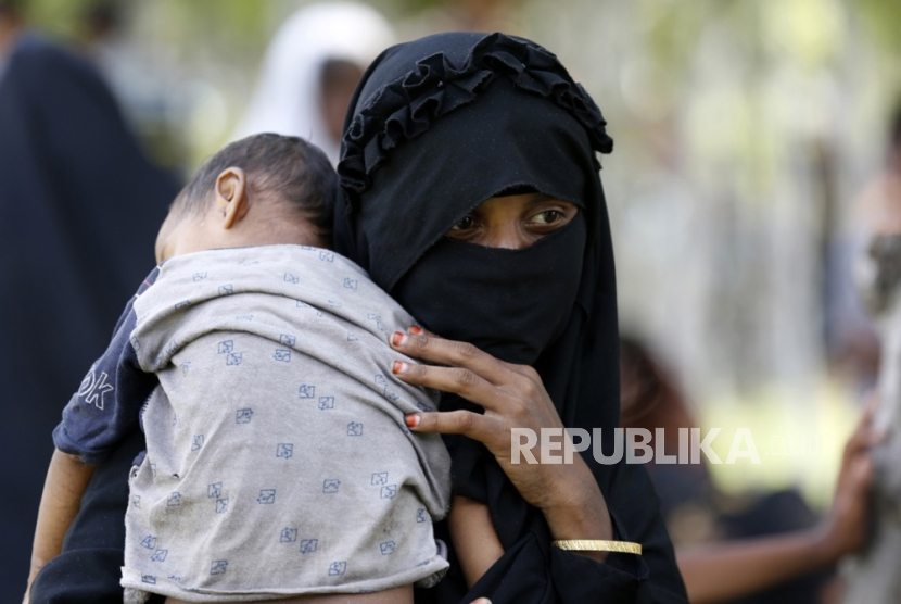 Seorang pengungsi Rohingya menggendong seorang anak saat ia dan orang lain beristirahat di area terbuka setelah mendarat di pantai di Desa Blang Ulam, Aceh Besar, Indonesia, 10 Desember 2023. 