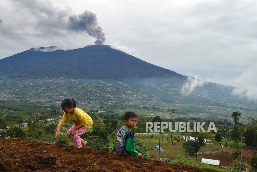 Anak-anak bermain di ladang saat Gunung Marapi mengeluarkan abu vulkanik.