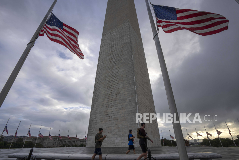 Orang-orang berjalan melewati bendera Amerika yang berkibar setengah tiang di sekitar Monumen Washington pada Senin, (11/9/2023). 