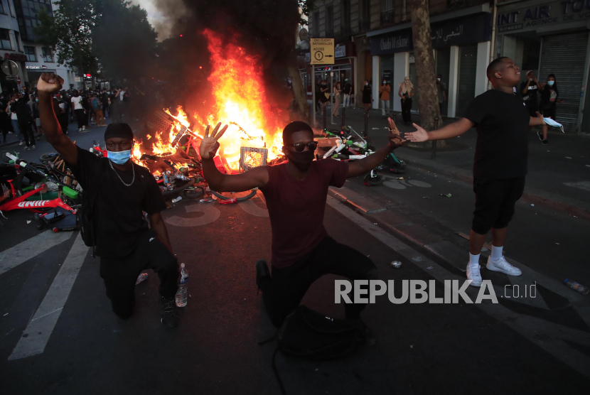 Sejumlah pengunjuk rasa berlutut di depan barikade yang terbakar saat demonstrasi di Paris, Selasa (2/6). Prancis larang warganya berdemonstrasi karena kekhawatiran penularan Covid-19.