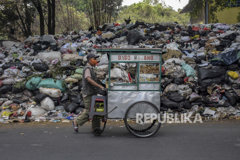 Pedagang melintas di samping tumpukan sampah di TPS Tegallega, Kota Bandung, Jawa Barat. Sebanyak 29 ribu ton masih tertahan di Kota Bandung akibat pembatasan TPA Sarimukti.