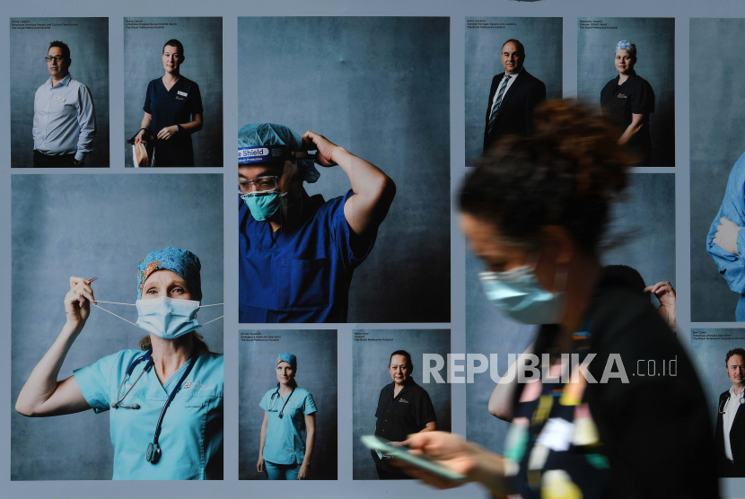 Pejalan kaki tampak mengenakan masker melewati pameran fotografi luar ruangan tentang petugas kesehatan di Melbourne, Australia, Selasa (22/9). Pemakaian masker penting untuk mencegah penyebaran dan penularan Covid-19.
