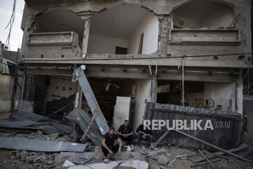 Warga Palestina duduk di depan rumah mereka yang rusak, ilustrasi