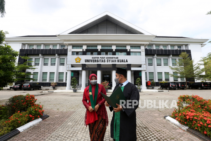 Wisudawan dan wisudawati berjalan di depan gedung rektorat Universitas Syiah Kuala (USK), Kota Banda Aceh, Provinsi Aceh, Jumat (4/6/2021). 