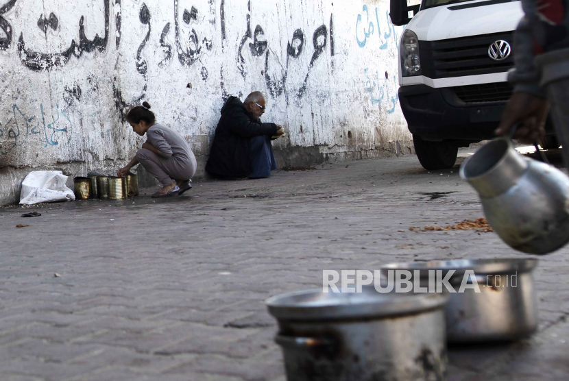 Pengungsi Palestina mengambil makanan dari panci logam saat yang lain menunggu untuk menerima bantuan makanan yang disediakan oleh kelompok pemuda Palestina di kamp pengungsi Rafah, Jalur Gaza Selatan, 25/1/2024.