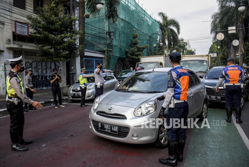 Petugas gabungan memeriksa pelat nomor kendaraan saat uji coba pemberlakuan ganjil genap di Jalan Asia Afrika, Kota Bandung, Jumat (13/8). Satlantas Polrestabes Bandung bersama Dishub Kota Bandung melakukan uji coba pemberlakuan ganjil genap di sejumlah ruas jalan protokol di Kota Bandung yang bertujuan untuk menekan mobilitas masyarakat guna meminimalisir penyebaran Covid-19 di masa perpanjangan PPKM Level 4. Foto: Republika/Abdan Syakura