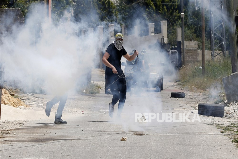 Palestinian protesters seek cover from tear gas during clashes with Israeli troops after a demonstration against Israel