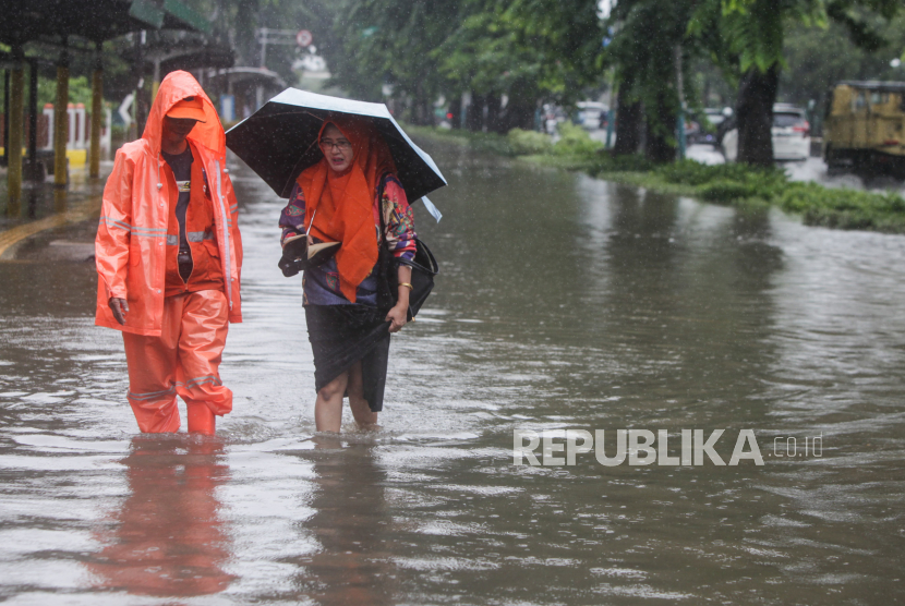 Petugas BPBD menuntun warga berjalan melewati genangan air di Jalan Letjen Suprapto, Cempaka Putih, Jakarta, Kamis (29/2/2024). Hujan deras yang mengguyur Jakarta sejak dini hari dan buruknya drainase membuat ruas jalur lambat pada jalan tersebut tergenang air.