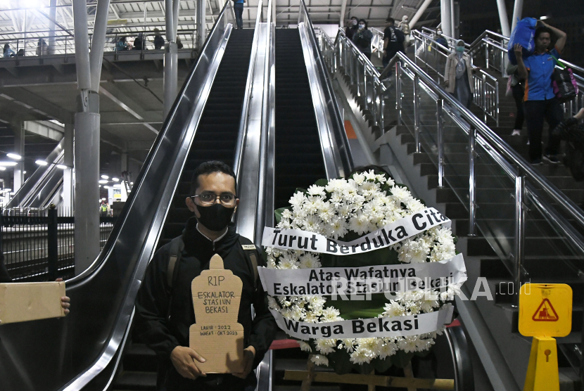 Seorang penumpang kereta melakukan aksi dengan membawa bunga bertuliskan turut berduka cita atas wafatnya satu eskalator di Stasiun Bekasi, Jawa Barat, Rabu (31/1/2024).