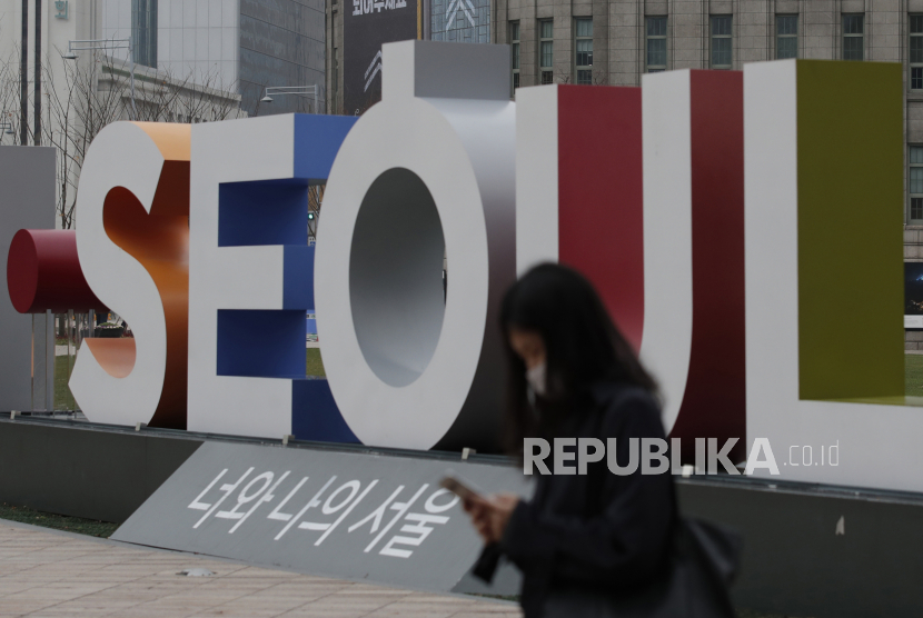  Seorang wanita yang mengenakan masker wajah sebagai pencegahan terhadap virus corona, berjalan di dekat tampilan logo ibu kota Korea Selatan Seoul di pusat kota Seoul, Korea Selatan, Rabu, 18 November 2020. 