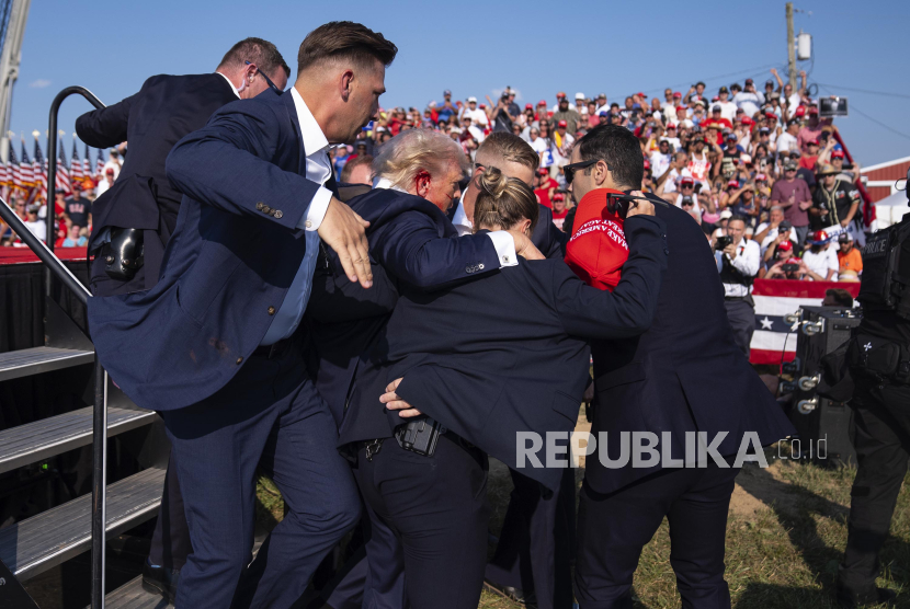 Kandidat presiden dari Partai Republik yang juga mantan Presiden Donald Trump dibantu turun panggung oleh agen Dinas Rahasia AS usai ditembak saat kamapnye di Butler, Pennsylvania, AS, Sabtu (13/7/2024). Kandidat Presiden dari Partai Republik Donald Trump terluka usai suara tembakan terdengar di tengah kampanye di Pennsylvania. Meskipun terluka, Trump dipastikan dalam kondisi baik.