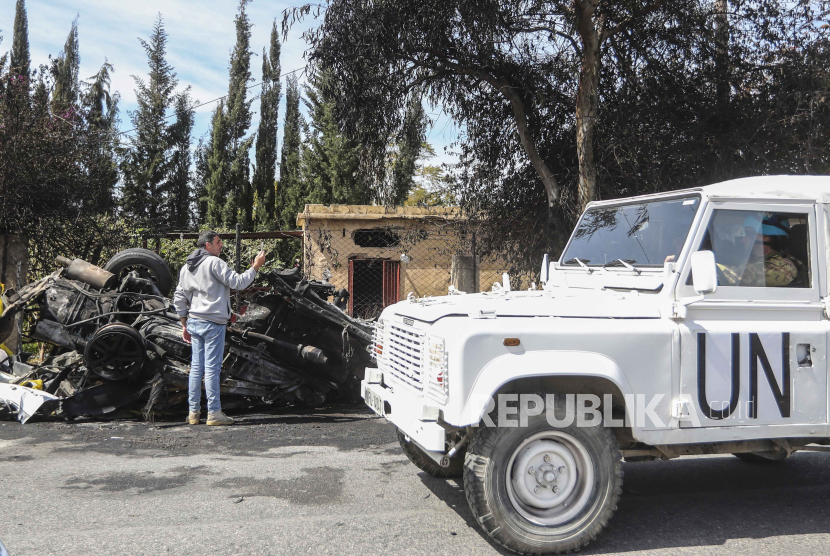 Kendaraan penjaga perdamaian PBB lewat di samping mobil yang hancur di pinggiran selatan Tyre, Lebanon, Rabu, (13/3/2024). 