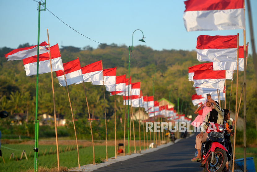 Warga berfoto dengan latar deretan ratusan bendera merah putih di Dukuh Dobangsan, Giripeni, Kulonprogo, Yogyakarta, Kamis (10/8/2023). Agenda rutin di pedukuhan Dobangsan saat menyambut HUT RI dengan memasang bendera merah putih di sepanjang jalan masuk kampung. Sekitar seribu bendera merah putih yang masih baru disiapkan oleh pengurus dusun untuk dipasang. Kemeriahan ini juga memancing warga luar dusun untuk datang dan berfoto-foto dengan latar belakang deretan bendera merah putih.