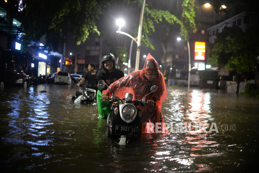 Pengendara mendorong motornya saat menerobos banjir di Jalan Kemang Raya, Jakarta Selatan.