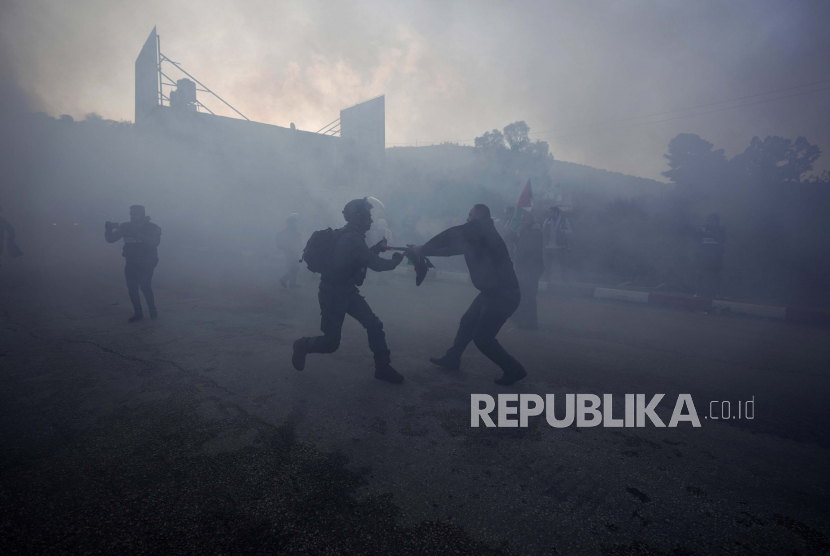 Seorang pengunjuk rasa Palestina dan seorang tentara Israel menarik bendera Palestina di tengah asap dari bom suara, selama demonstrasi setelah pemukim Yahudi mencoba untuk memblokir anak-anak Palestina memasuki sekolah di desa al-Lubban al-Sharqiya, dekat kota Tepi Barat. Nablus, Minggu, 27 Februari 2022. Jurnalis Palestina Ditembak Mati Pasukan Israel di Hari Pertama Bekerja