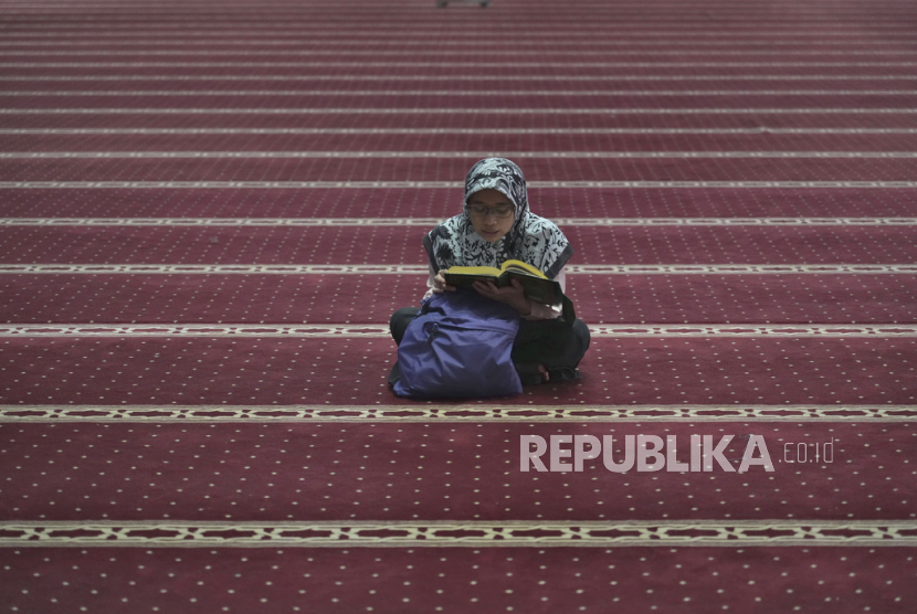  Seorang muslimah membaca Alquran sambil menunggu waktu berbuka puasa di hari pertama Ramadhan di Masjid Istiqlal di Jakarta, Kamis (23/3/2023).