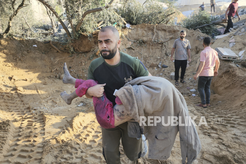 Warga Palestina membawa seorang anak yang tewas dalam serangan udara Israel di Deir el-Balah Jalur Gaza, pada 15 Oktober 2023.